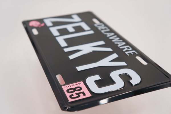 A black license plate with white lettering and pink numbers.