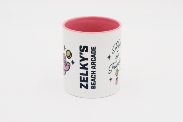 A pink and white coffee mug with the words " zelky 's beach arcade " on it.